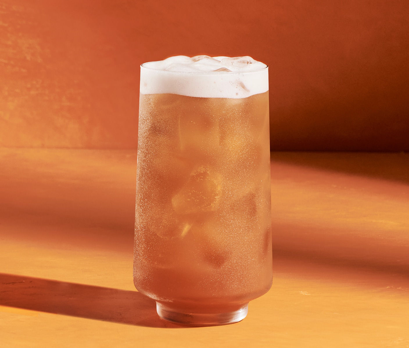 Une boisson orange glacée servie dans un verre avec une couche de mousse.