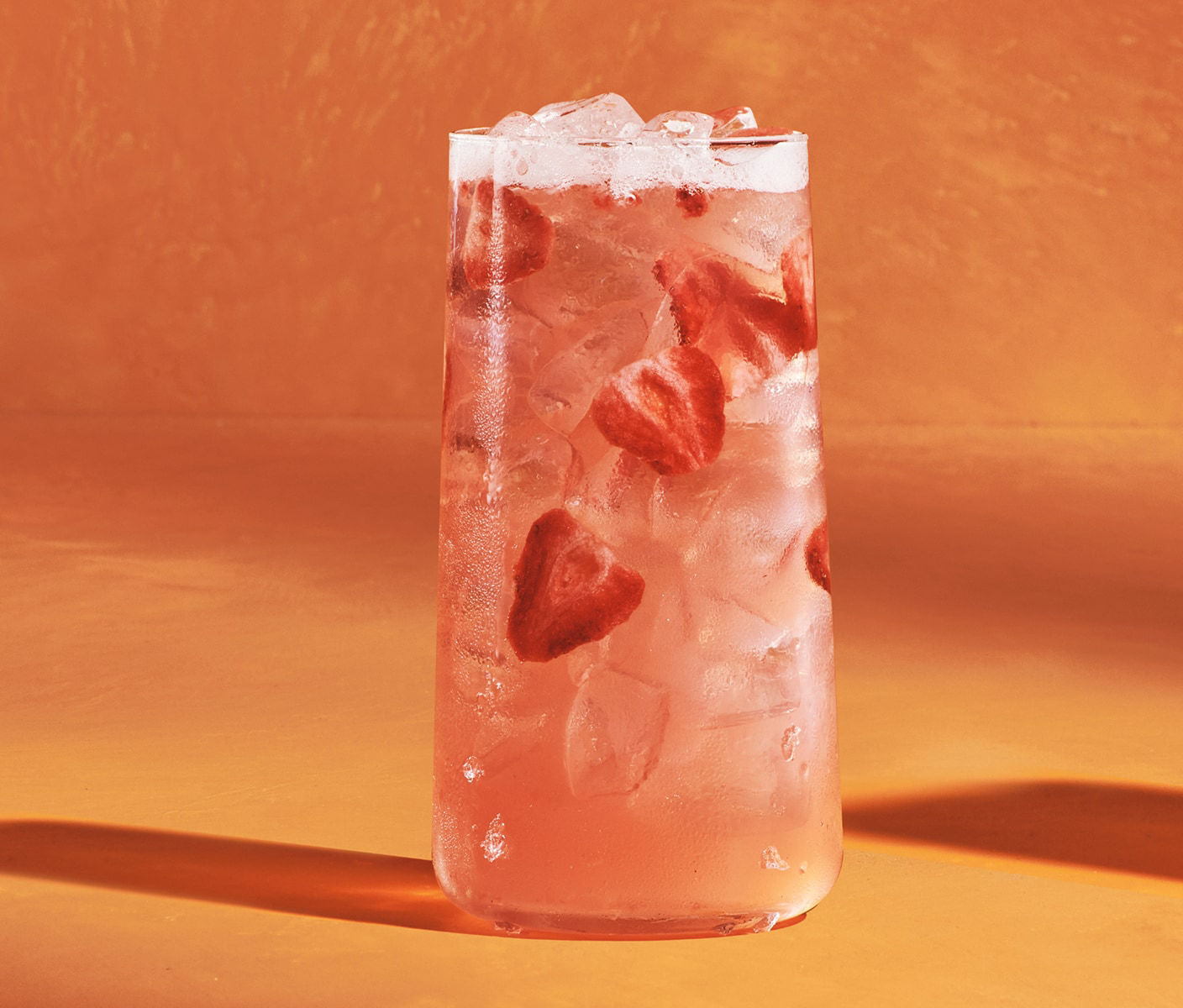 Une boisson rose glacée servie dans un verre avec des morceaux de fraises.