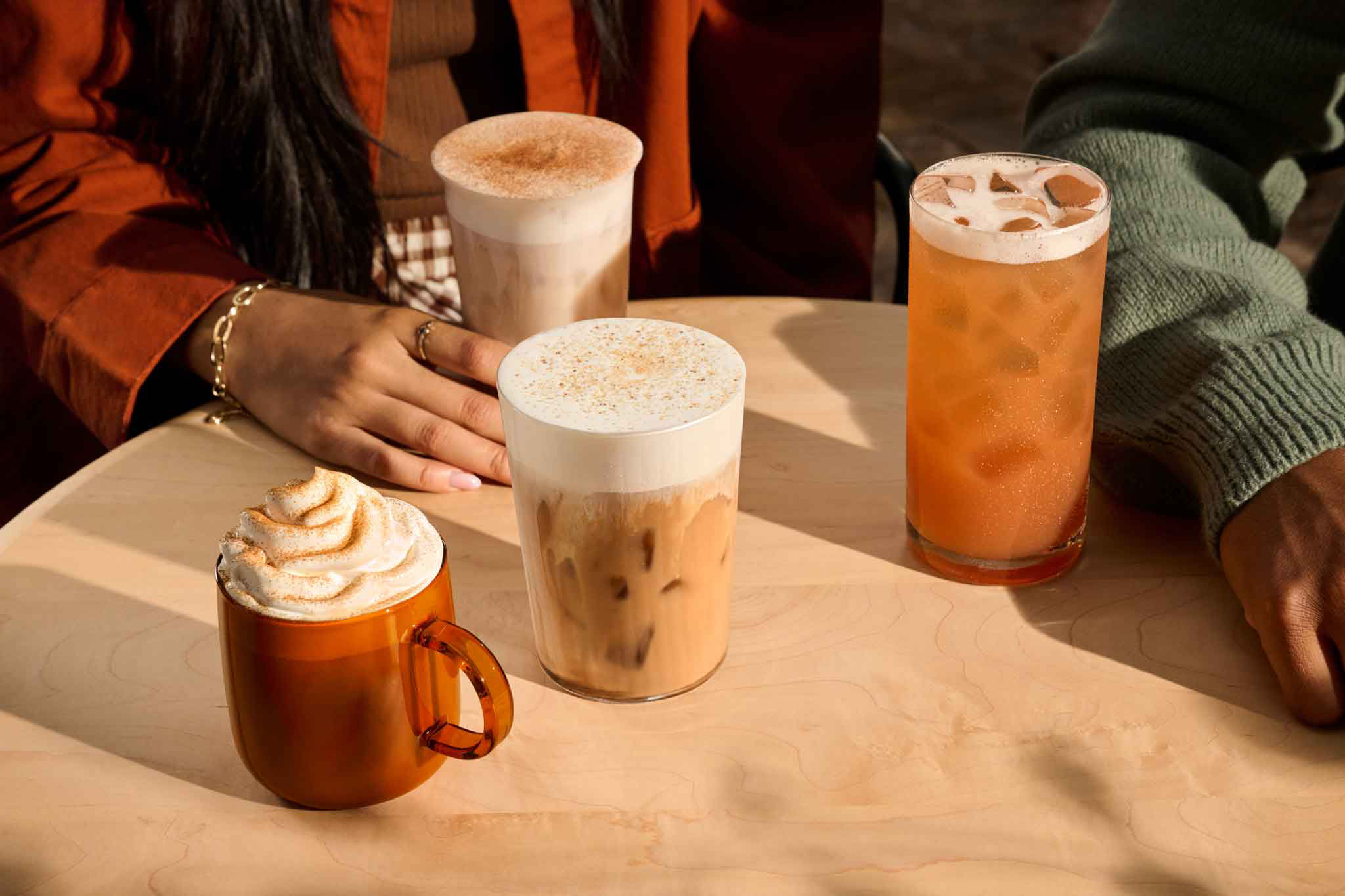 Quatre boissons d’automne posées sur une table autour de laquelle des personnes sont rassemblées.